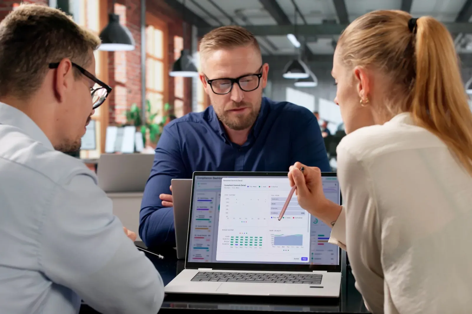 Three colleagues reviewing a compliance dashboard on a laptop in an office